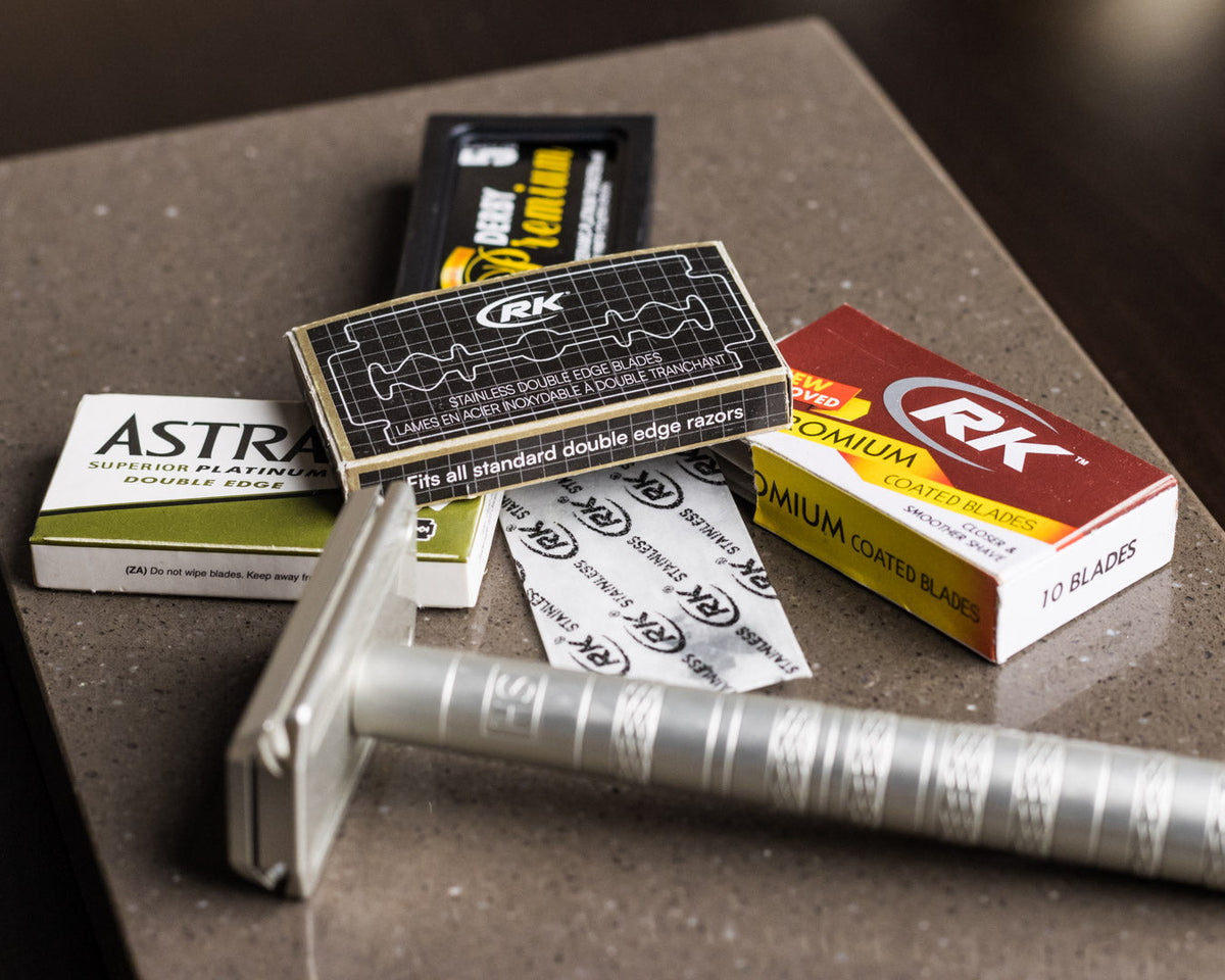 The Henson AL13 safety razor and various brands of double edged razor blades laid out on a quartz slab.